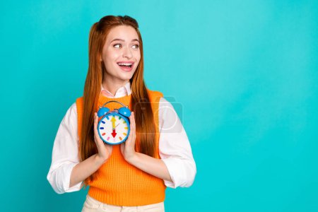 Photo of cheerful lovely adorable woman wear trendy orange clothes hold clock bell look empty space isolated on cyan color background.