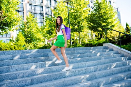 Foto de hermosa chica de buen humor vestida ropa de uniforme de moda subiendo escaleras campus universitario al aire libre estilo urbano.