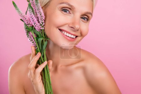 Foto von fröhlich liebenswert nette Seniorin natürliche Creme Lotion Balsam Anti-Age-Effekt isoliert auf rosa Hintergrund.