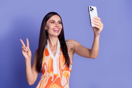 Photo de dame brillante douce porter robe tache selfie dispositif moderne isolé fond de couleur violette.