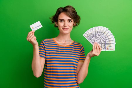 Foto-Porträt der attraktiven jungen Frau halten Kreditkartengeld Fan gekleidet stilvolle gestreifte Kleidung isoliert auf grünem Hintergrund.