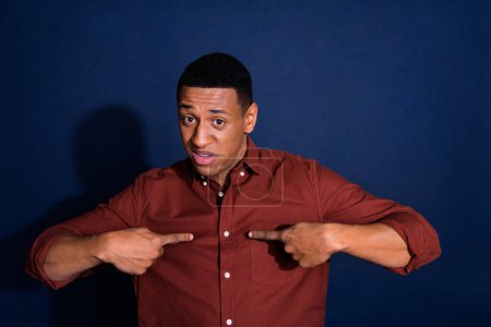 Photo of young man point fingers himself wear brown shirt isolated on dark blue color background.