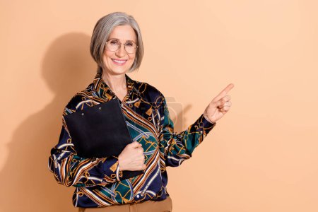 Portrait of positive woman dressed print shirt in glasses hold clipboard indicating empty space isolated on pastel color background.