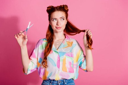Photo of cute girl dressed colorful blouse look at red tail in arm hold scissors changing hairstyle isolated on pink color background.
