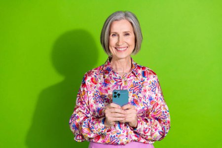 Photo of positive confident lady dressed pink shirt communicating modern device empty space isolated green color background.