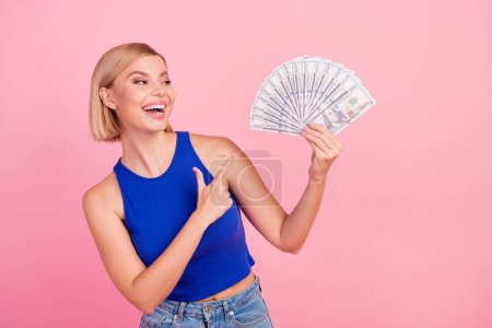 Photo of pretty young woman point finger money wear blue top isolated on pink color background.