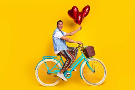 Full length photo of ecstatic guy dressed jeans waistcoat riding on cycle in empty space hold bubbles isolated on yellow color background.