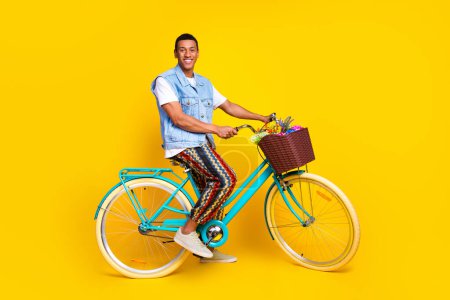 Full length photo of good mood guy dressed jeans waistcoat sit on cycle riding in empty space isolated on vibrant yellow color background.