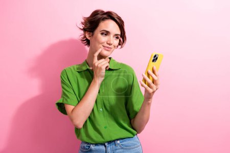 Photo of pretty cute young woman dressed green shirt finger chin texting modern gadget isolated pink color background.