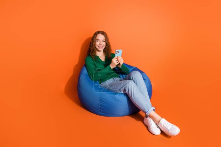 Full length photo of cute sweet lady dressed green shirt communicating modern device isolated orange color background.