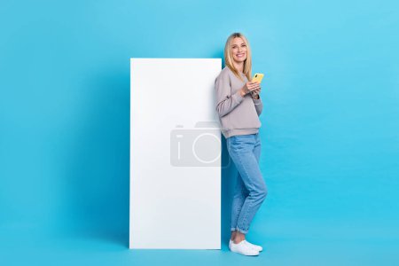 Full length photo of pretty lady wear stylish clothes empty space satisfied cool gadget device isolated on blue color background.
