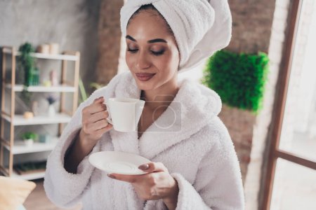 Portrait photo de attrayant jeune femme tenir tasse boire thé tête enveloppé serviette habillée peignoir de bain intérieur profiter week-end.
