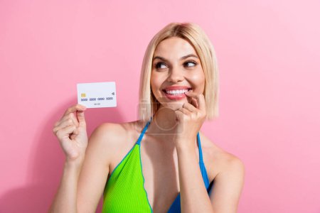 Portrait of minded smart woman wear colorful top holding debit card look at proposition empty space isolated on pink color background.