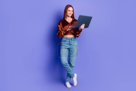 Foto von hübscher junger Frau mit Laptop-Netzwerk in voller Länge tragen braunes Hemd isoliert auf violettem Hintergrund.