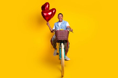 Full length photo of optimistic impressed guy dressed jeans waistcoat ride on cycle hold bubbles isolated on yellow color background.