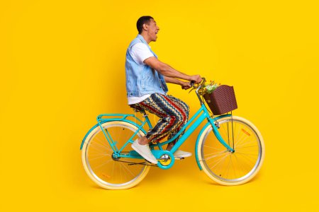 Full length photo of astonished guy dressed jeans waistcoat driving cycle look empty space isolated on vibrant yellow color background.
