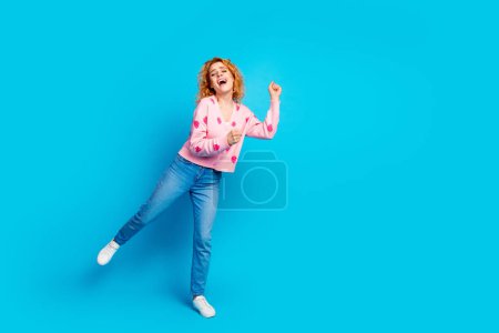 Full length photo of attractive young woman dancing have fun dressed stylish pink clothes isolated on blue color background.