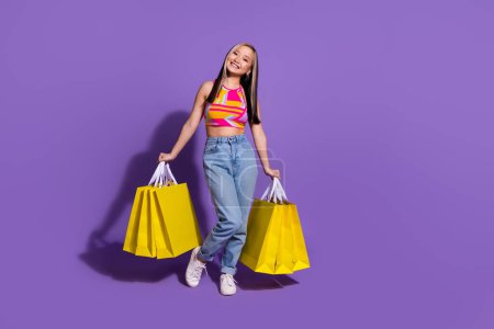Foto de longitud completa de adorable linda chica desgaste de moda tienda de ropa centro comercial compra aislada sobre fondo de color púrpura.