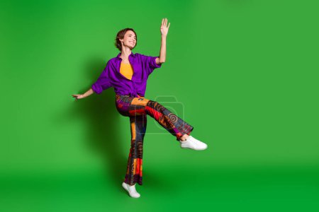 Foto von positiven jungen Frau in lila stilvolles Hemd trendige Vintage-Hosen in der Diskothek isoliert auf grünem Hintergrund.