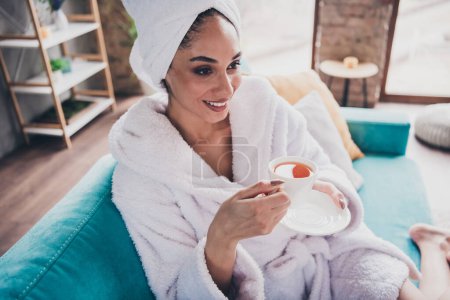 Portrait photo de jolie jeune fille assise canapé boisson thé tenir tasse tête enveloppé serviette habillée peignoir beauté routine concept maison.