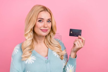 Photo of positive smart nice woman with wavy hairdo dressed print cardigan fingers hold debit card isolated on pink color background.