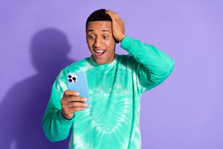 Photo of handsome impressed guy wear teal sweatshirt getting likes modern gadget isolated purple color background.