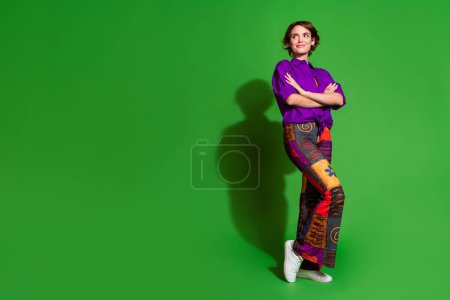 Foto de cuerpo entero de una hermosa mujer joven en traje vintage de moda doblado manos buscando idea creativa aislada en el fondo de color verde.