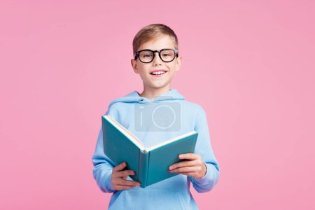Portrait of cute clever positive schoolkid toothy smile hold opened book isolated on pink color background.
