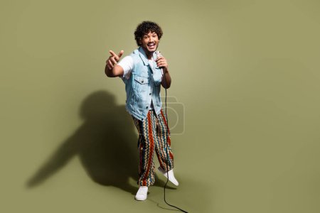 Full body photo of attractive young man sing microphone karaoke have fun dressed stylish denim clothes isolated on khaki color background.