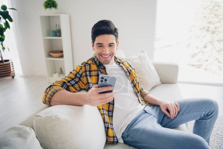 Photo of funky positive man wear checkered shirt staying home reading news modern device indoors house apartment room.