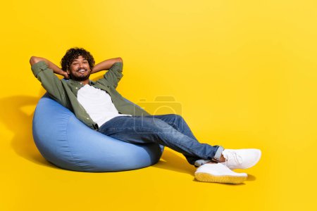 Portraitfoto von jungen lustigen mexikanischen Kerl in khakifarbenem Hemd liegend Sitzsack träumt von einem besseren Leben isoliert auf gelbem Hintergrund.