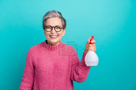 Photo of satisfied woman with short hair dressed pink sweater in glasses hold sprayer cleaning house isolated on teal color background.