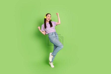 Full body photo of attractive young woman headphones dancing dressed stylish striped violet clothes isolated on green color background.