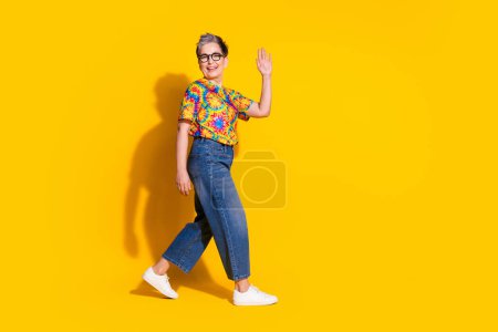 Foto de encantadora mujer mayor usar ropa de impresión de moda hola signo aislado sobre fondo de color amarillo vivo.
