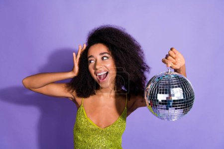 Photo portrait of gorgeous young girl dancing hold discoball wear trendy green sequins outfit isolated on purple color background.
