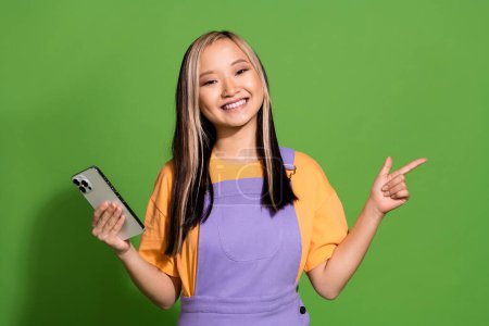 Portrait photo de jolie jeune fille tenir dispositif point vide espace porter tenue jaune violet tendance isolé sur fond de couleur verte.