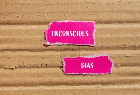 Unconscious bias words written on ripped pink paper pieces with cardboard background. Conceptual unconscious bias symbol. Copy space.