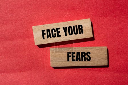Stellen Sie sich Ihren Ängsten mit Worten, die auf Holzklötzen mit rotem Hintergrund geschrieben sind. Konzeptionell stellen Sie sich Ihren Ängsten. Kopierraum.