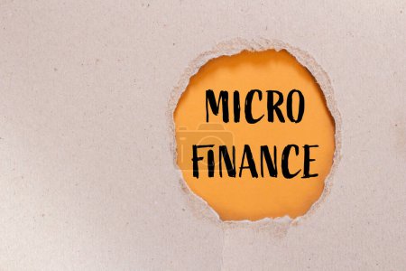 Palabras de micro finanzas escritas en papel rasgado con fondo naranja. Símbolo conceptual del negocio de microfinanzas. Copiar espacio.