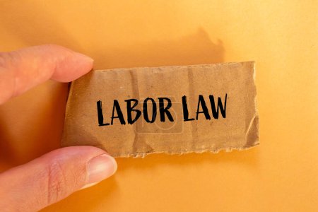 Mots du droit du travail écrits sur du papier cartonné déchiré avec fond orange. Symbole conceptuel du droit du travail. Espace de copie.