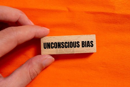 Unconscious bias words written on wooden block with orange background. Conceptual unconscious bias symbol. Copy space.