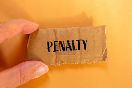 Penalty word written on ripped cardboard paper piece with orange background. Conceptual penalty symbol. Copy space.