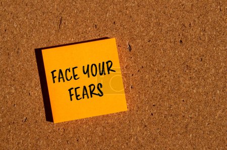 Faites face à vos craintes mots écrits sur un autocollant en papier orange avec fond brun. Conceptuel face à vos craintes symbole. Espace de copie.