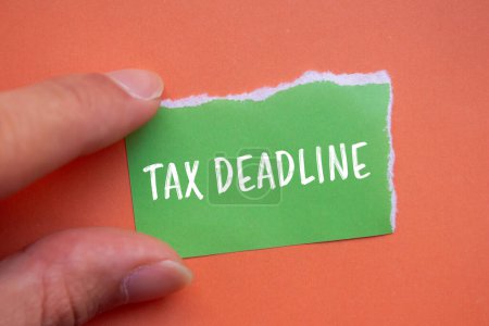 Mots de délai d'impôt écrits sur papier vert déchiré avec fond orange. Symbole conceptuel de délai fiscal. Espace de copie.