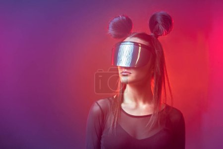 Porträt der schönen Cyber-Model Frau posiert mit futuristischer Brille auf dem Kopf und Neonlicht in einer virtuellen Tech-Umgebung