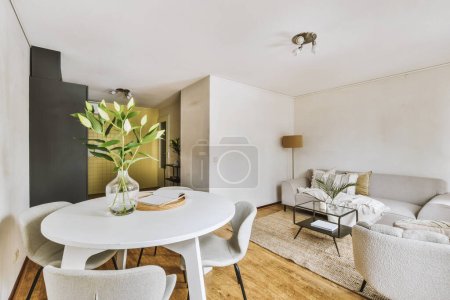 Table en bois minable avec chaises et vase situé près du canapé confortable contre les murs clairs avec décorations et TV dans un appartement moderne