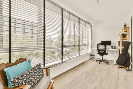 una sala de estar con suelos de madera y persianas blancas en las ventanas que dan a un área de escritorio de oficina