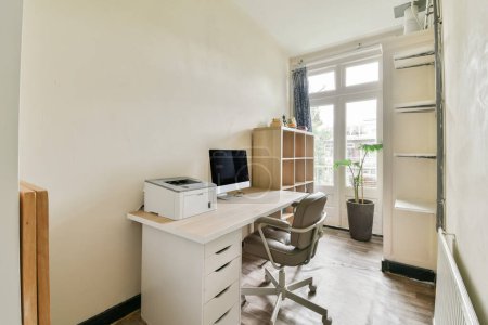 Photo for A room with a desk, chair and computer on the wall next to it is a window that looks out onto an outside view - Royalty Free Image