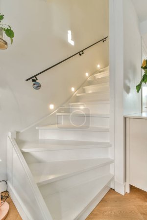 una escalera blanca en una casa con pisos de madera y luminarias en la pared detrás de ella es una puerta abierta