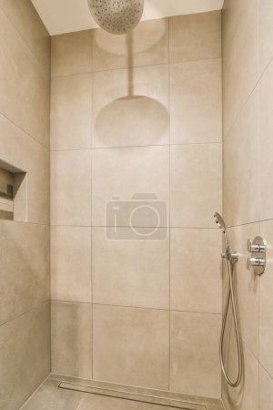 Photo for A shower room with beige tiles on the walls and floor, there is a hand held shower head in the corner - Royalty Free Image